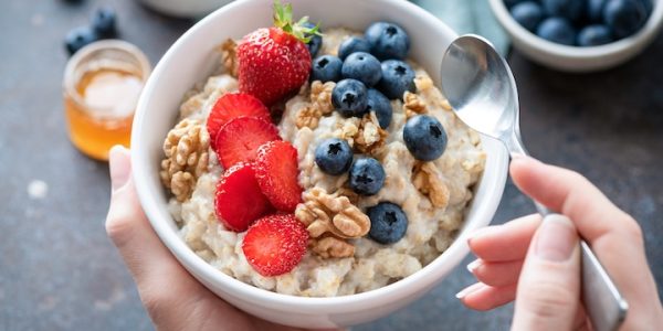 Oatmeal porridge bowl with berry fruits in female hands Oatmeal porridge bowl with berry fruits in female hands, closeup view. Healthy vegetarian breakfast food